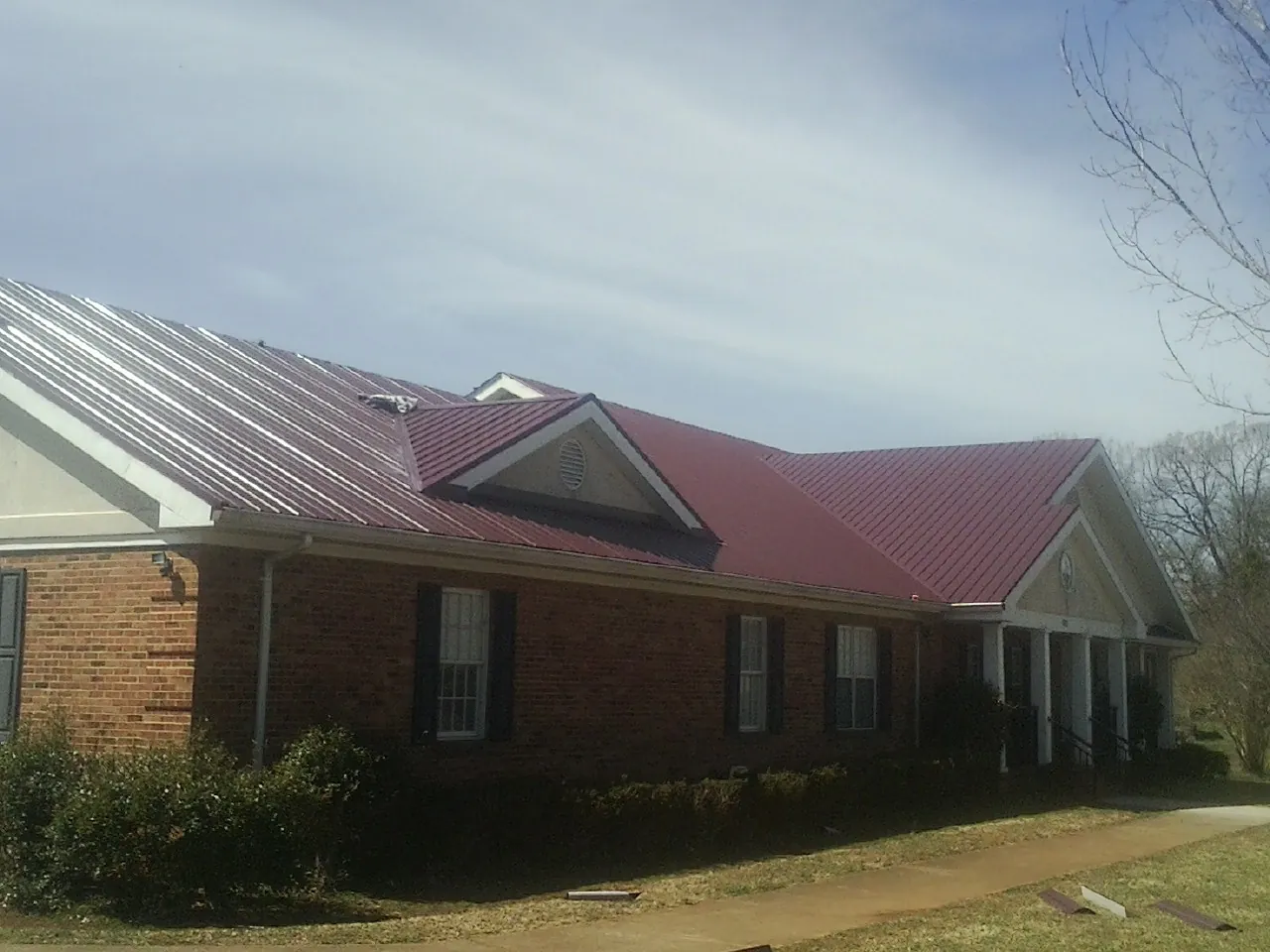 Red metal roof with gabled entries on a long brick building, from a Hail Damage Roof Repair job in Spangler