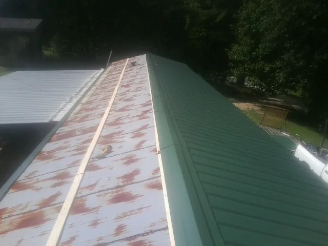 Old rusted panels beside newly installed green metal roofing — Wind Damage Roof Repair by Roofing Brothers in Spangler