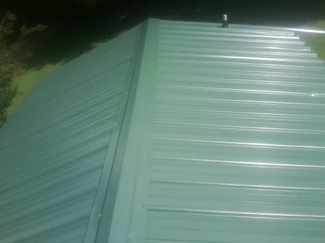 New green metal panels meeting at the ridge of a roof — Flat Roof Repair work by our crew in Spangler