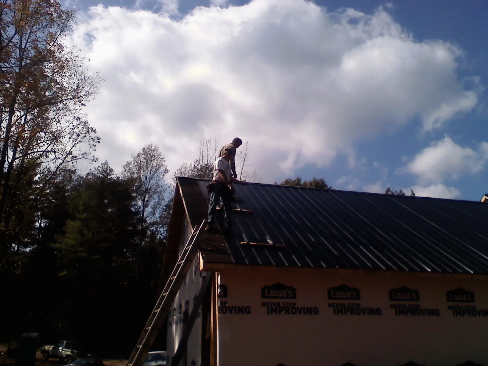 Roofer fastening dark metal panels high against a cloudy sky, from a Roof Inspection job in Spangler