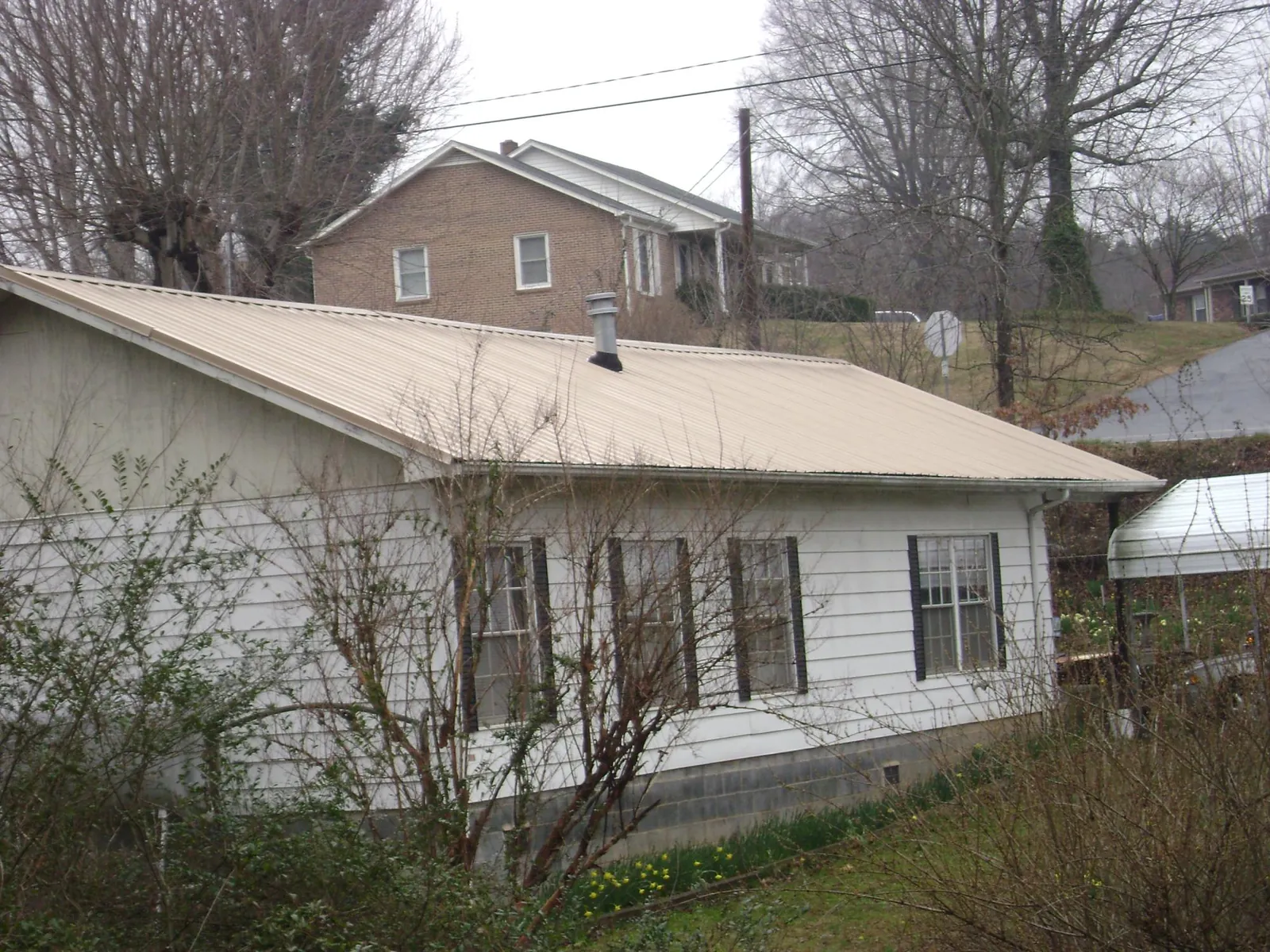 Tan metal roof on a white sided house set into a hillside — Commercial Roofing by Roofing Brothers in Spangler