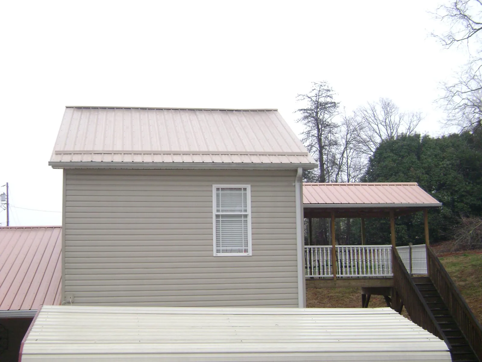 Tan metal roofs on a two story addition and attached porch, from a Roof Replacement job in Spangler